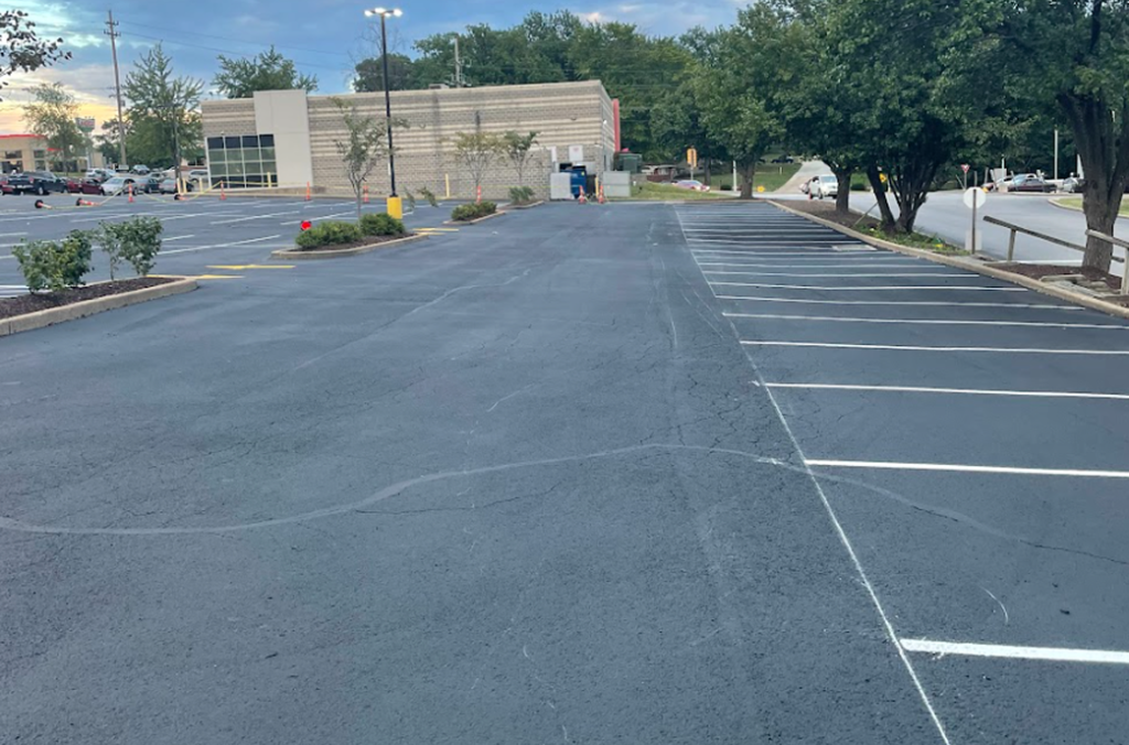 A mostly empty commercial asphalt parking lot with freshly painted lines, a few parked cars, trees along the edges, and a modern building in the background under a cloudy sky in St. Louis, MO.